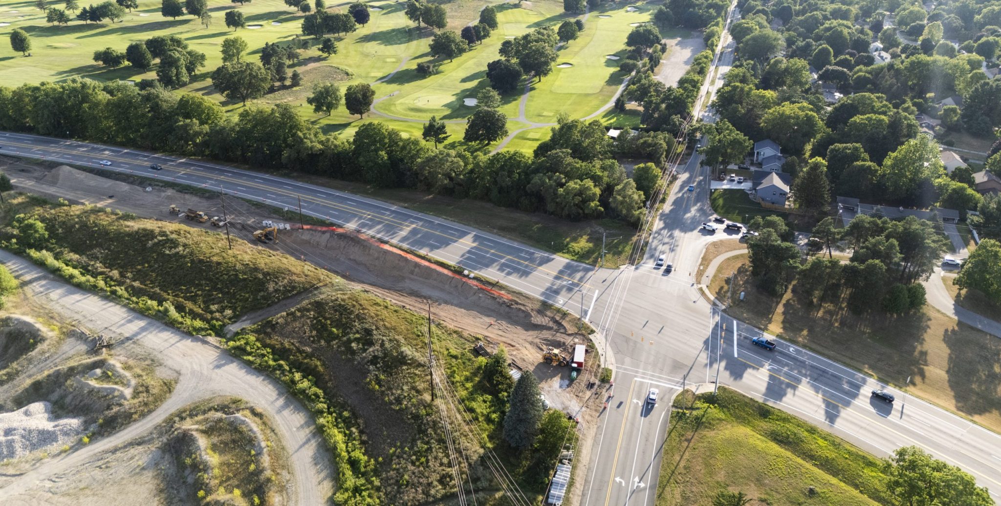 Aerial view of trail construction along a busy intersection with a golf course in the background