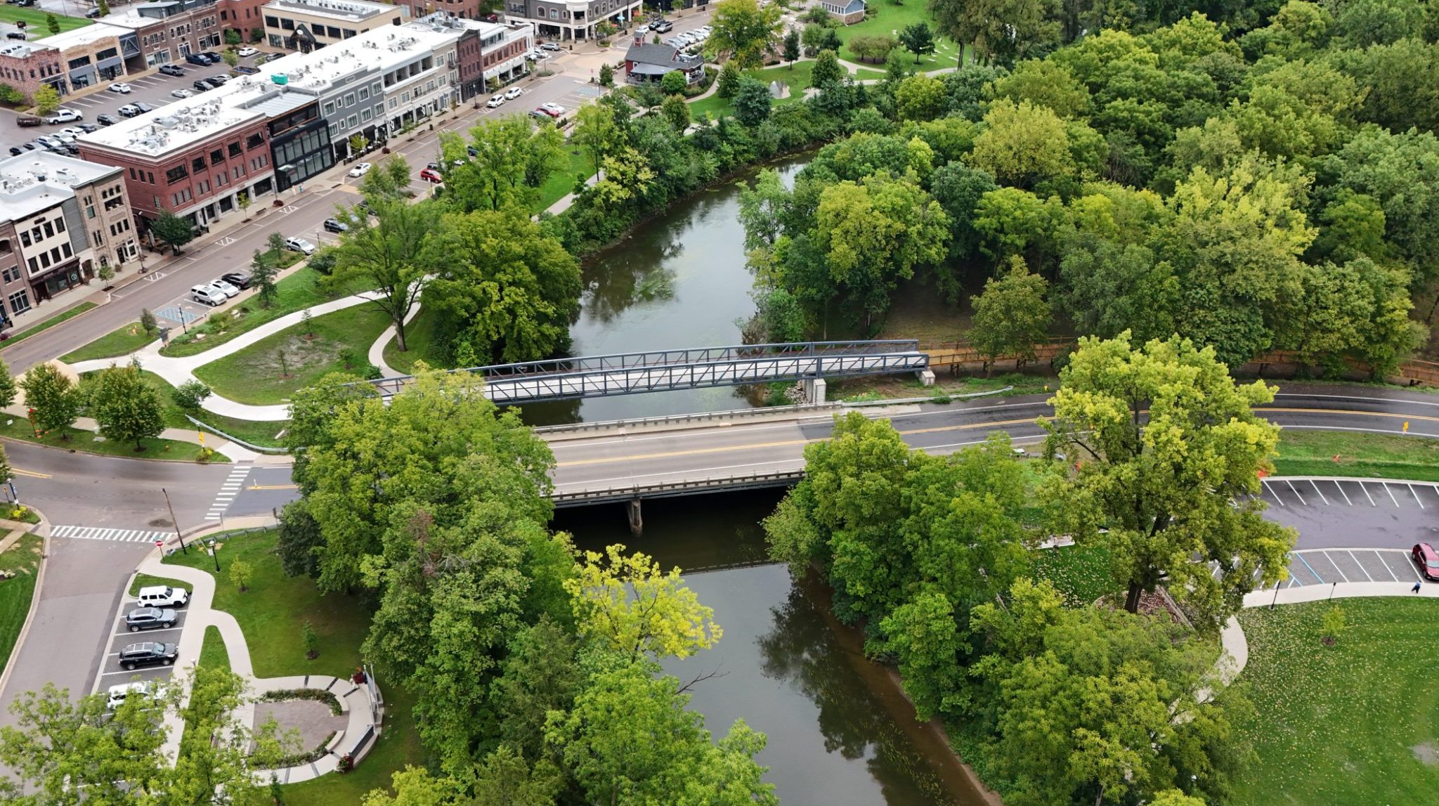 Aerial view of a pedestrian bridge next to a road surrounded by parks and trees